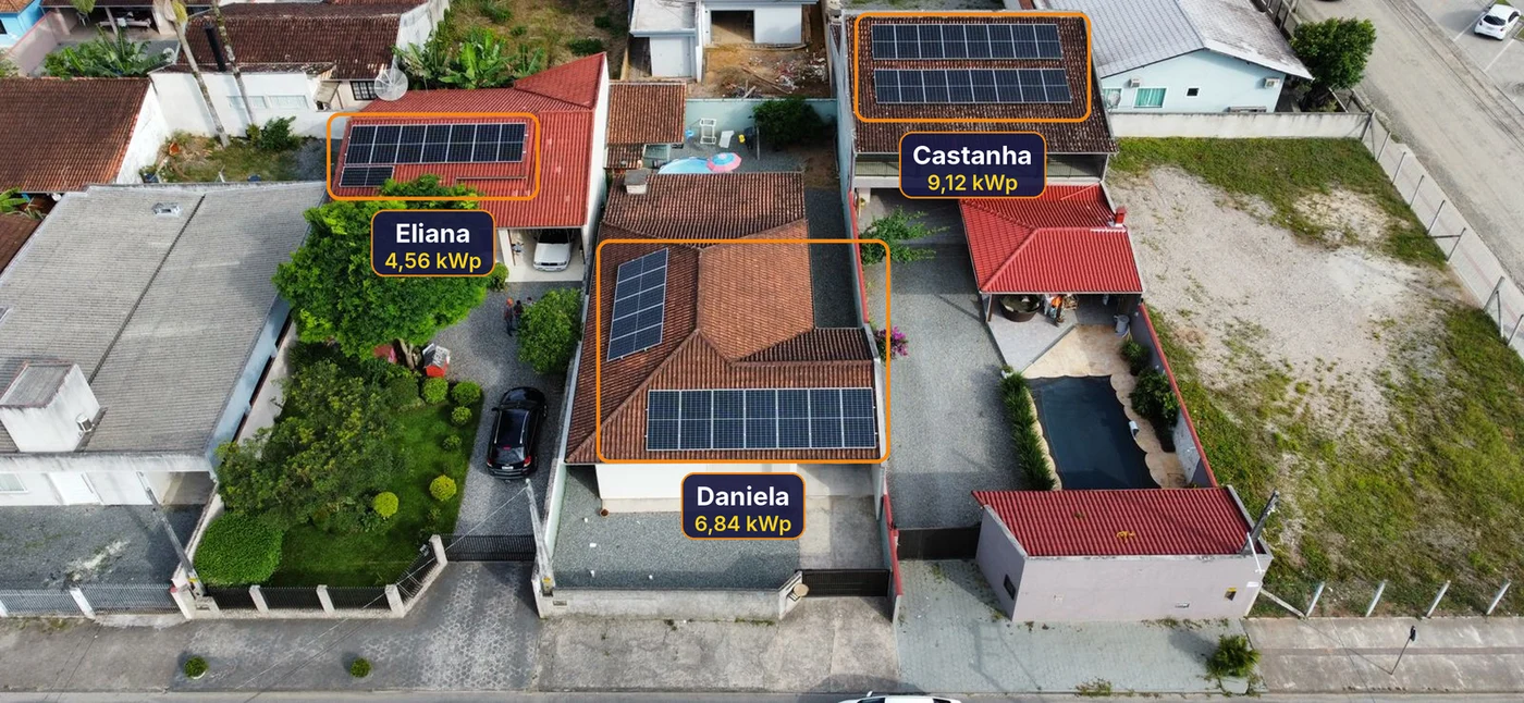 Vista aérea de três casas vizinhas em Joinville com painéis solares, cada uma marcada com um selo de sol